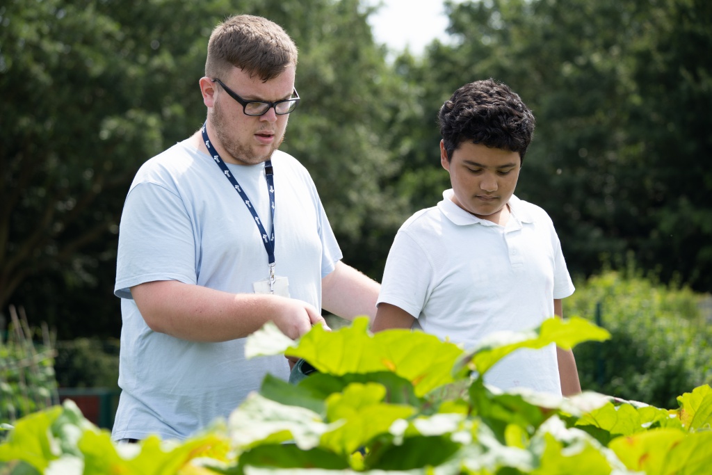 A young boy is accompanied by an adult member of staff, as they walk around the academy grounds together.