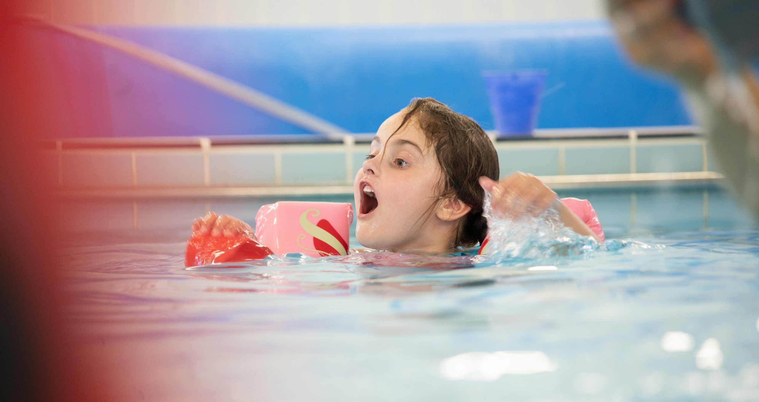 A young girl is pictured swimming in a pool and wearing pink armbands.