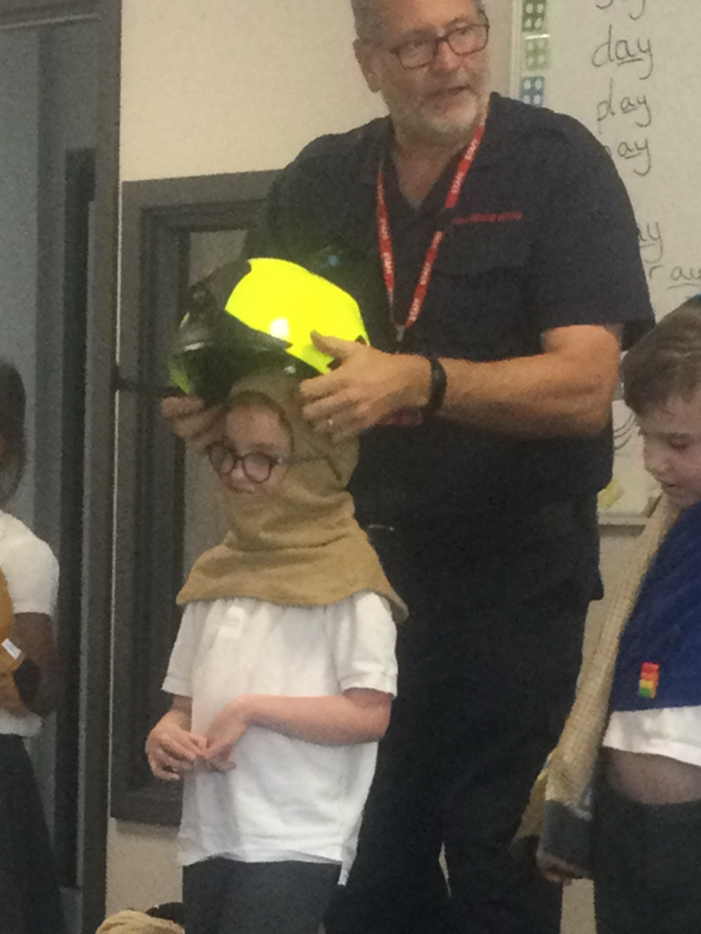 A Fireman visiting the school is seen adjusting a Fireman's helmet on a young student's head.