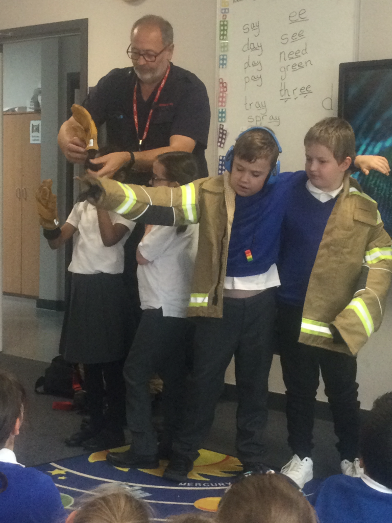 Four young students are seen trying on Fireman's uniform, under the supervision of a Fire Service staff member.