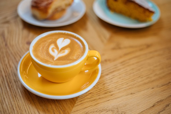 A cup of Coffee is seen sitting on a saucer on a table, alongside some cakes.