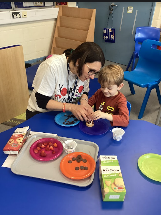 A member of staff is seen assisting a young boy to decorate some biscuits he has made.