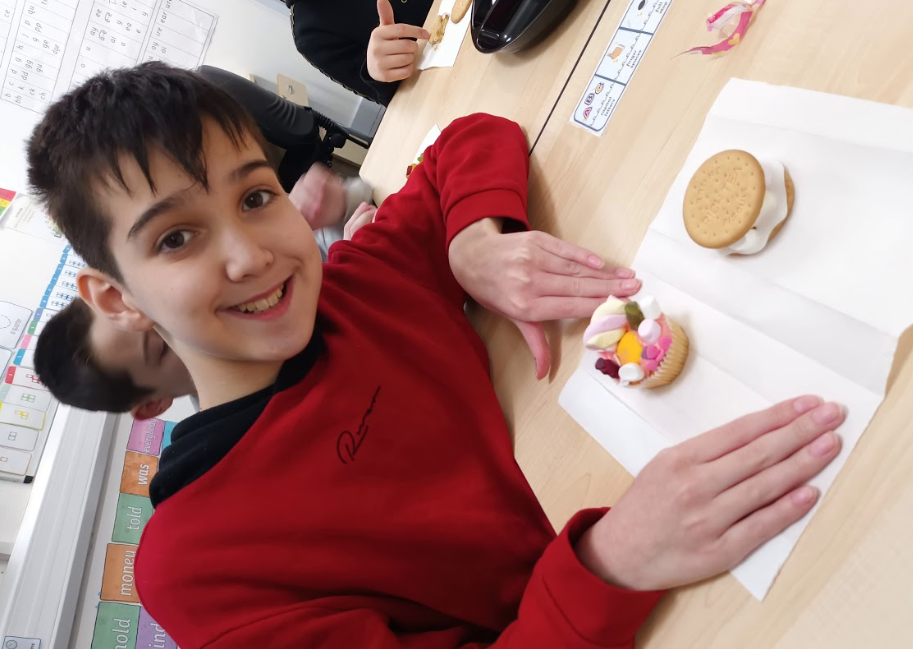 A boy is seen smiling for the camera alongside some cupcakes and biscuits he has baked.