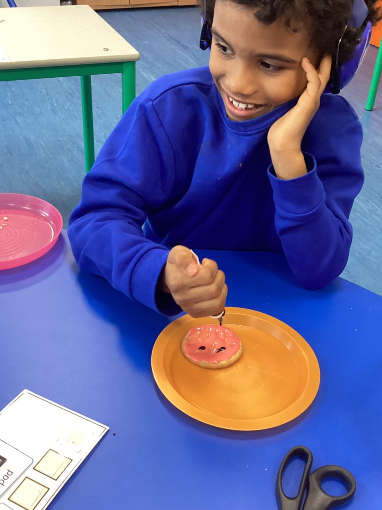 A young boy is seen smiling whilst decorating some biscuits he has baked.