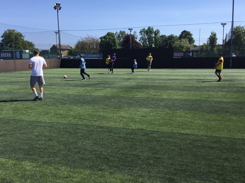 A team of students are pictured playing Football together, outdoors on an astro turf on the academy grounds.