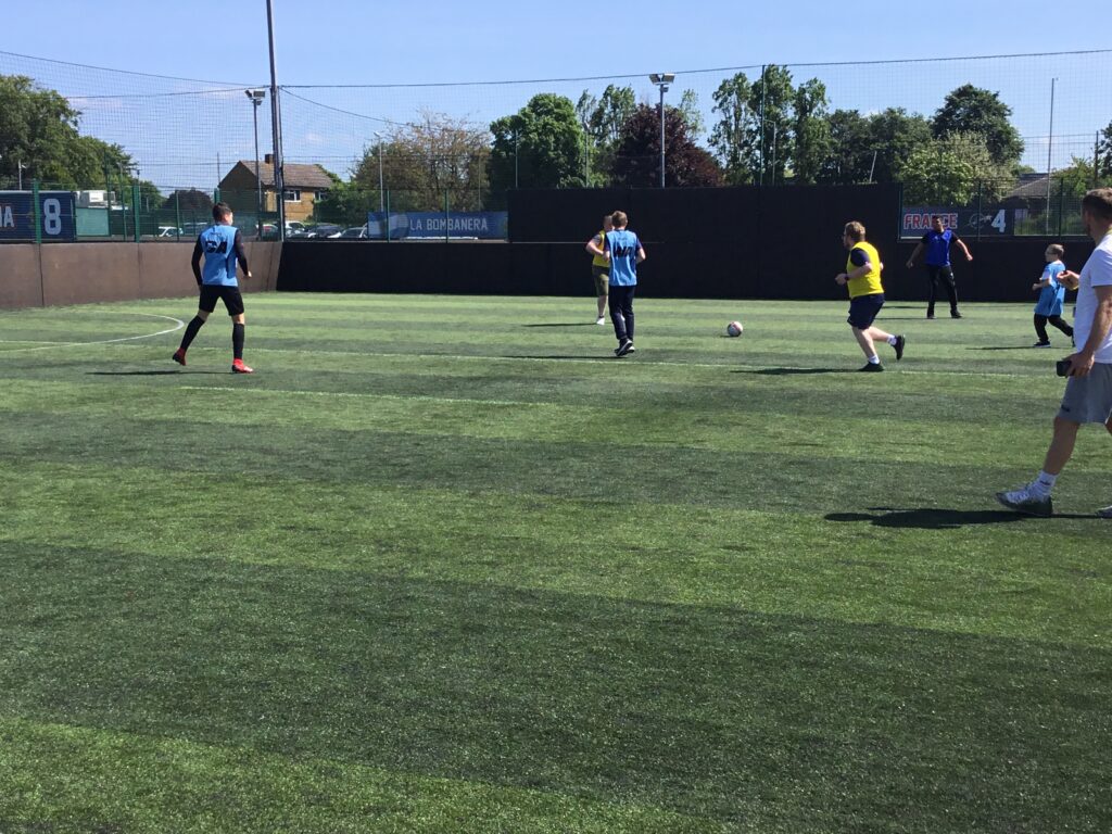 A team of students are pictured playing Football together, outdoors on an astro turf on the academy grounds.