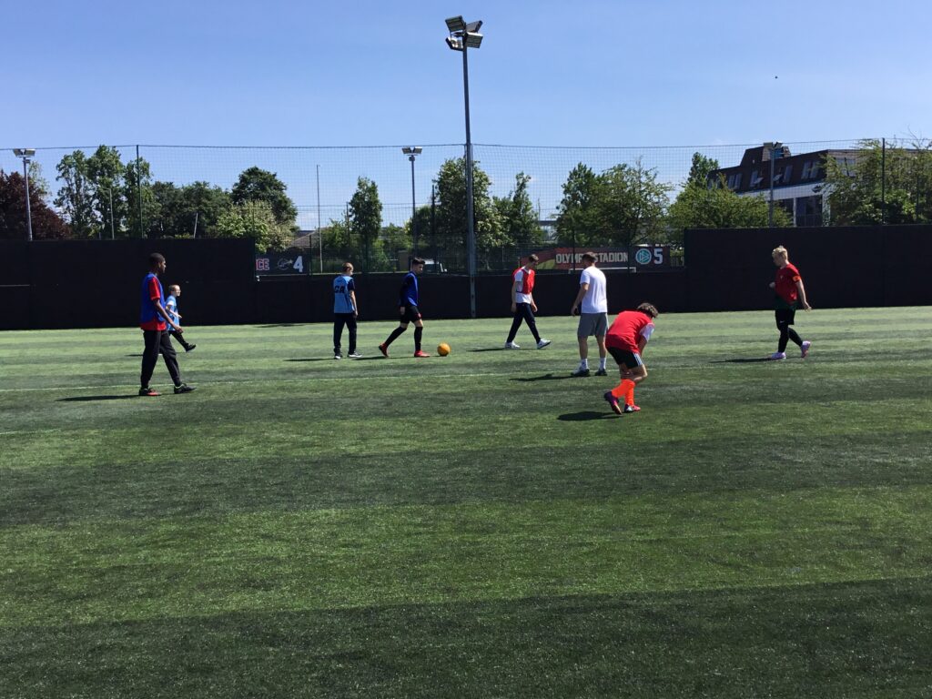 A team of students are pictured playing Football together, outdoors on an astro turf on the academy grounds.