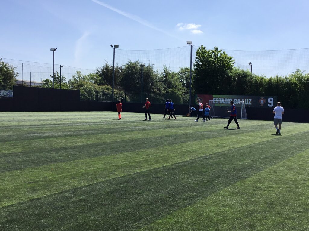 A team of students are pictured playing Football together, outdoors on an astro turf on the academy grounds.