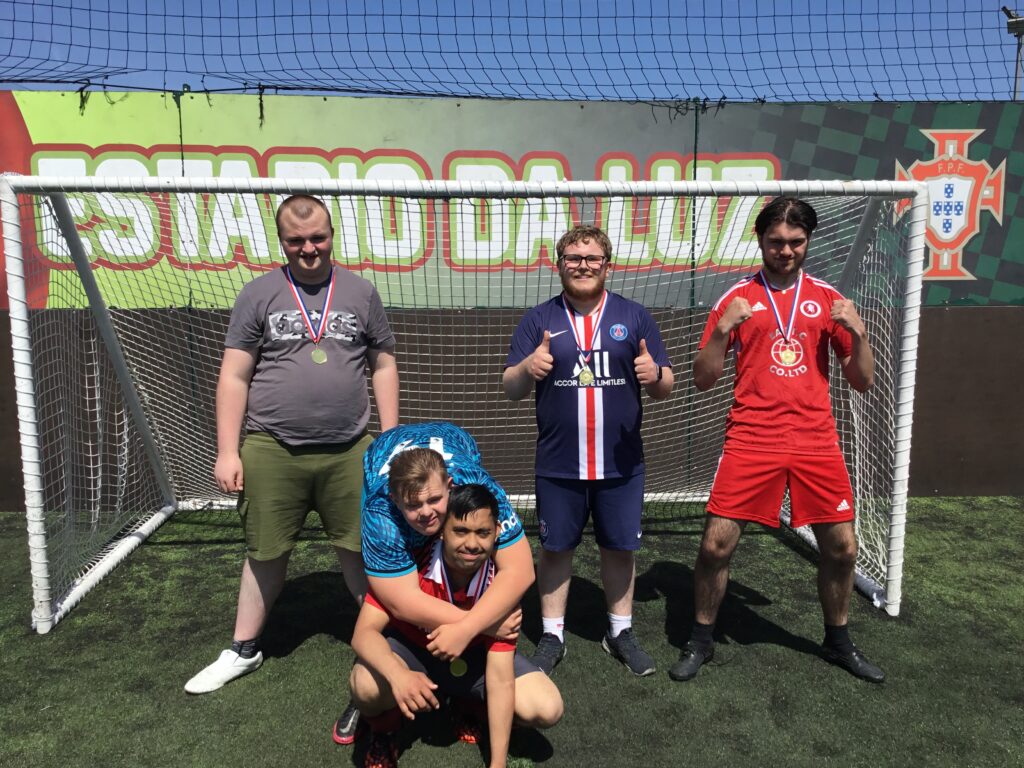 A small group of students are seen dressed up in their Football kit and celebrating for the camera, after having just won a prized trophy for their Football success.