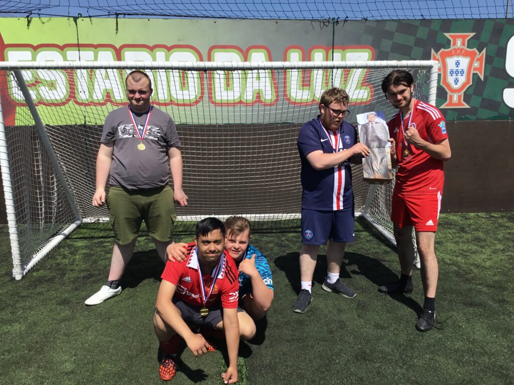 A small group of students are seen dressed up in their Football kit and celebrating for the camera, after having just won a prized trophy for their Football success.