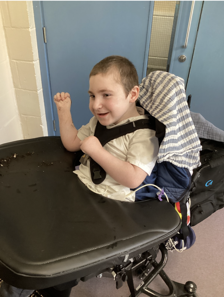 A young boy can be seen smiling at the camera, whilst sitting in his wheelchair in a corridor in the academy building.