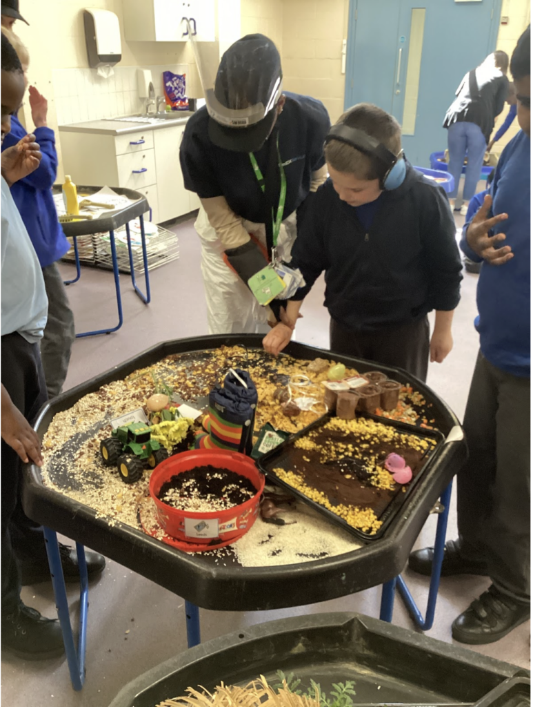 A young pupil is pictured playing with a toy farm set on a desk in front of him, whilst under the supervision of a member of staff.