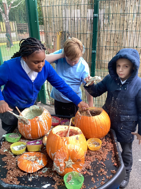 Three Milestone Academy students are pictured playing outdoors together, whilst scooping out the flesh of some Pumpkins, ready for carving.