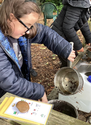 A female student is pictured using some saucepans to hold soil outside in the forest, alongside her peers.