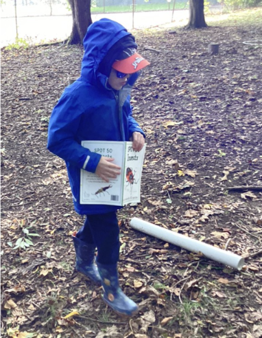 A young male student is pictured wearing his winter coat outdoors in the forest, whilst holding a book in his hands all about insects.