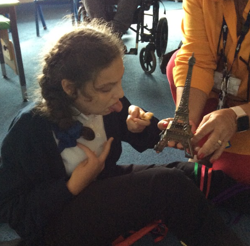 A young girl is pictured sat at a table, looking closely at a model of the Eiffel Tower being held by a member of staff.