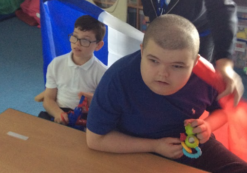 Two young, male students are pictured sat in their seats, paying attention to the front of the class.