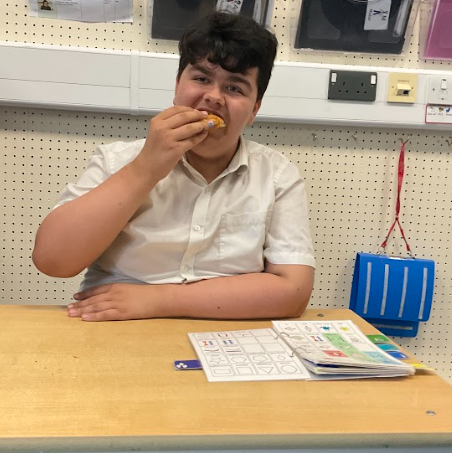 A male student is pictured snacking, whilst sat at his desk waiting to learn.