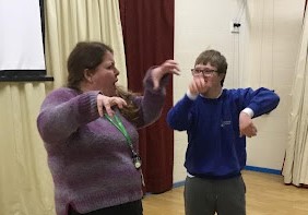 A young male student is pictured being taught sign language by a female member of staff.