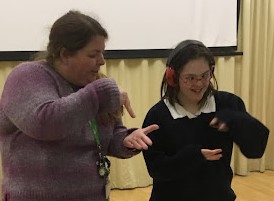 A young female student is pictured being taught sign language by a female member of staff.