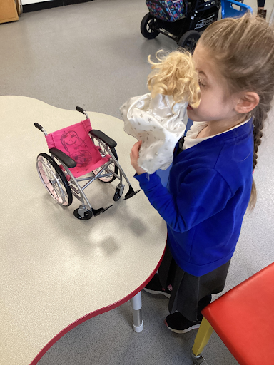 A young girl is pictured playing with a toy doll, about to place it into a wheelchair in celebration of International Wheelchair Day.